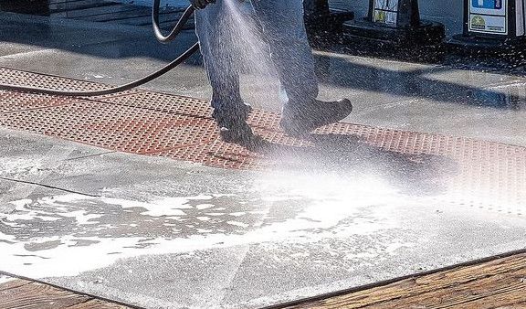A worker uses a pressure washer to clean a sidewalk outside a dining facility.