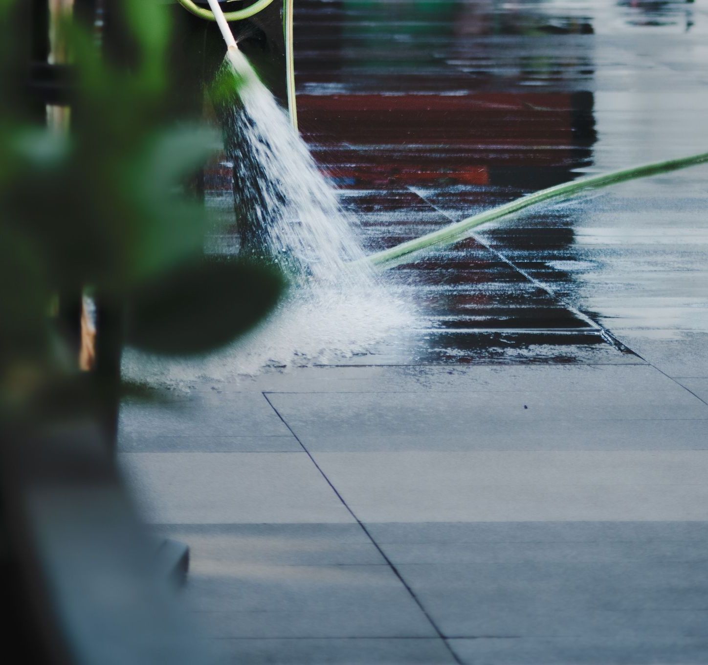A worker cleans a pavement with a hose beside a large white sculpture in urban setting.