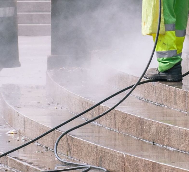 A street worker pressure washes stone stairs in a public park, ensuring cleanliness and safety.